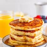 The Best Buttermilk Pancakes stacked on white plate with butter and syrup.