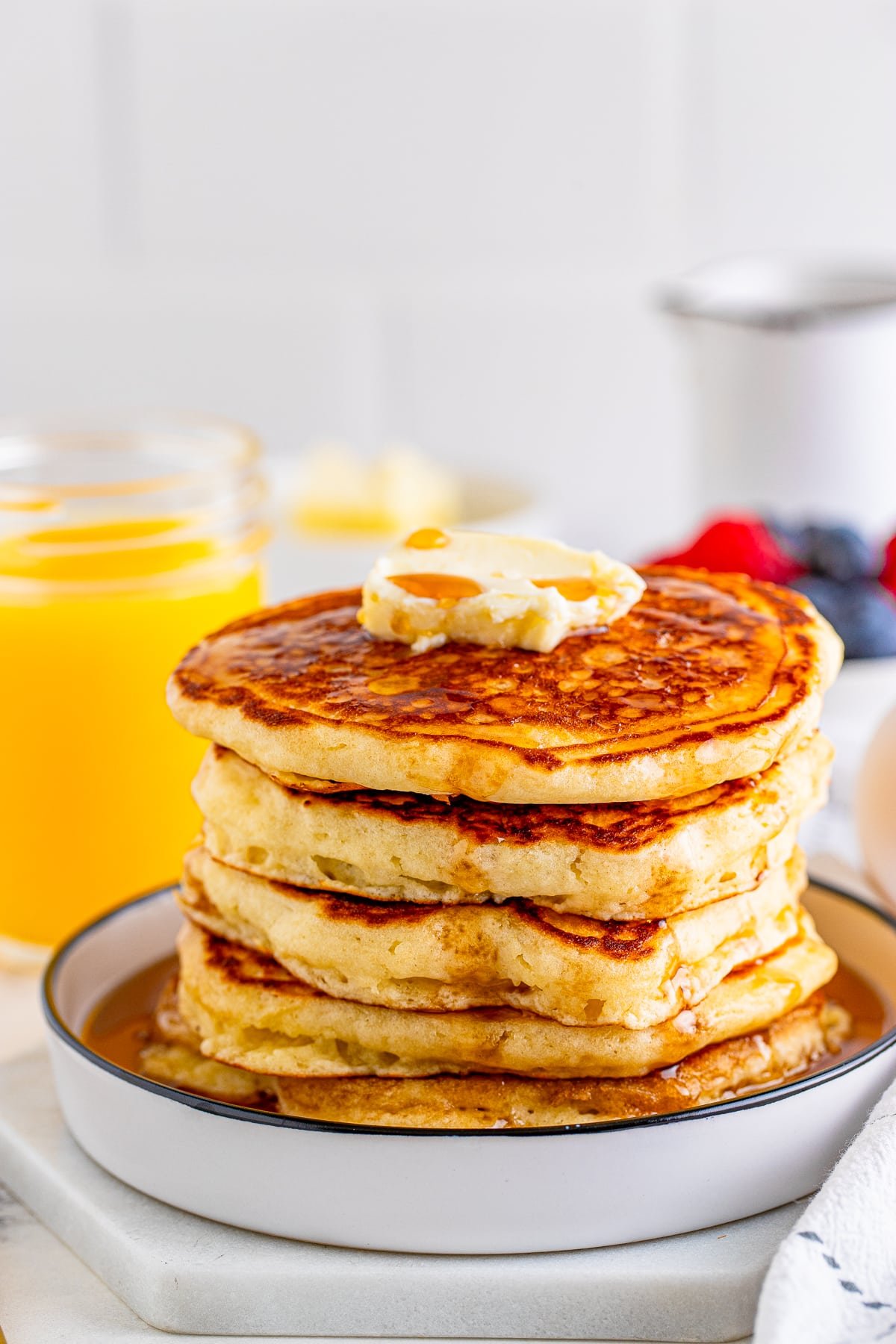 The Best Buttermilk Pancakes stacked on white plate with butter and syrup.