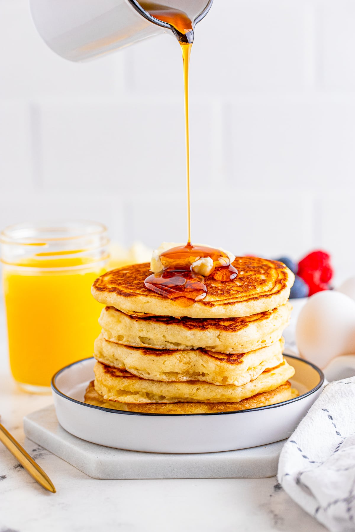 Syrup being poured over the stack of pancakes on white plate.