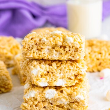 Three of the Rice Krispies Treats Recipe stacked on parchment paper with milk in background.