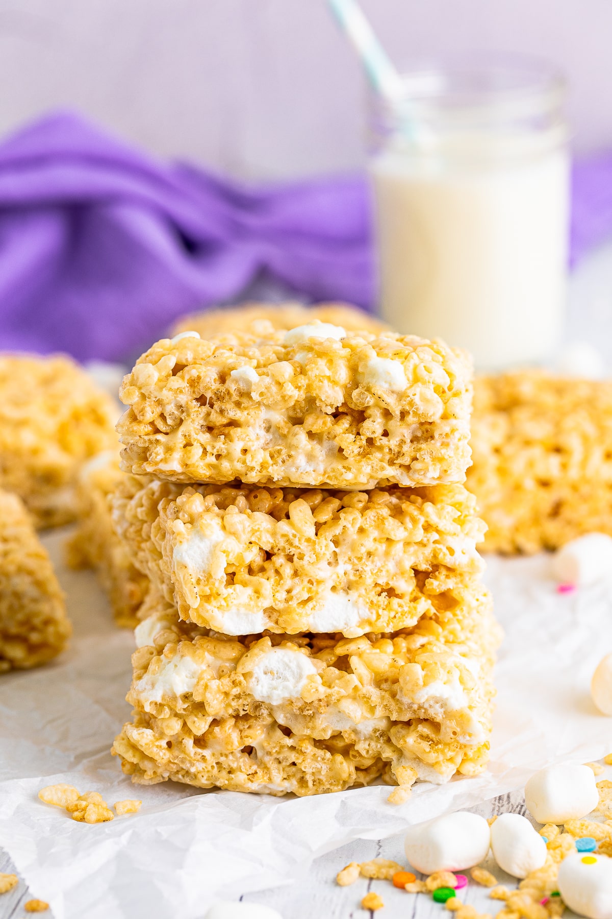 Three of the Rice Krispies Treats Recipe stacked on parchment paper with milk in background.