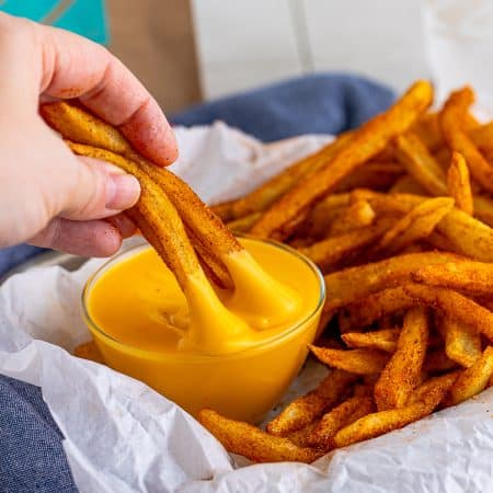 Nacho Fries Recipe being dipped into nacho sauce.