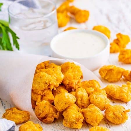 Popcorn Chicken in parchment paper on white wooden board with dipping sauce on back.
