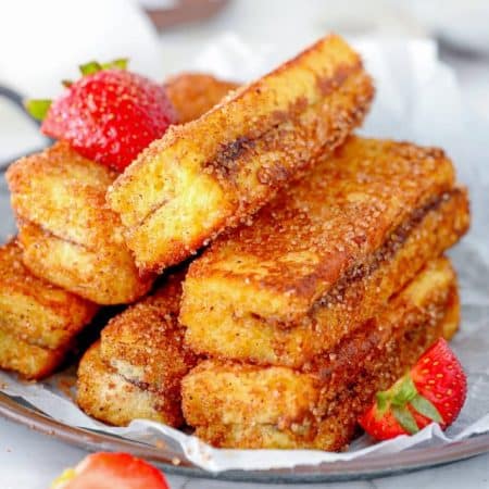 Stacked Nutella French Toast Sticks on plate with some sliced strawberries.