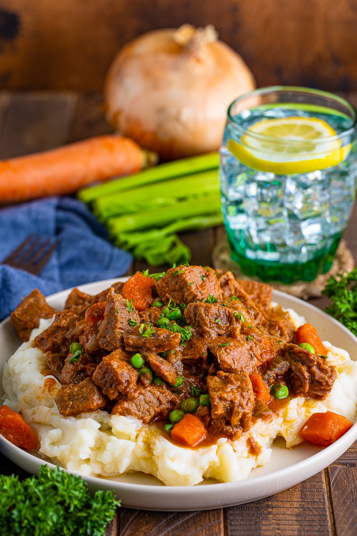 Easy Beef Stew over mashed potatoes with produce and water in background.