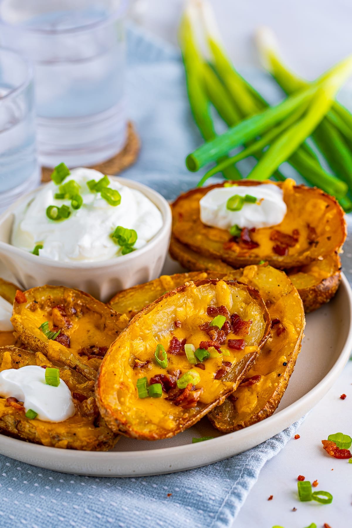 Finished Loaded Potato Skins on white plate with toppings and sour cream for dipping on side.