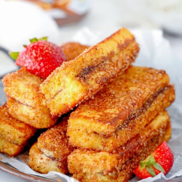 Stacked Nutella French Toast Sticks on plate with some sliced strawberries.