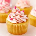 A vanilla Valentines Day Cupcake topped with a swirl of pink buttercream and pink pearl sprinkles.