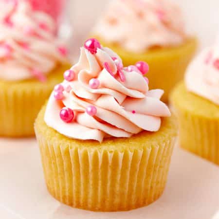 A vanilla Valentines Day Cupcake topped with a swirl of pink buttercream and pink pearl sprinkles.