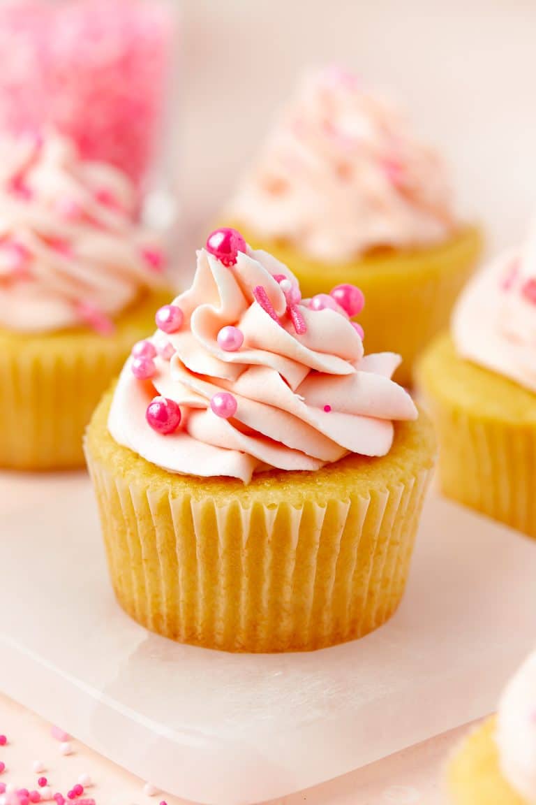 A vanilla Valentines Day Cupcake topped with a swirl of pink buttercream and pink pearl sprinkles.