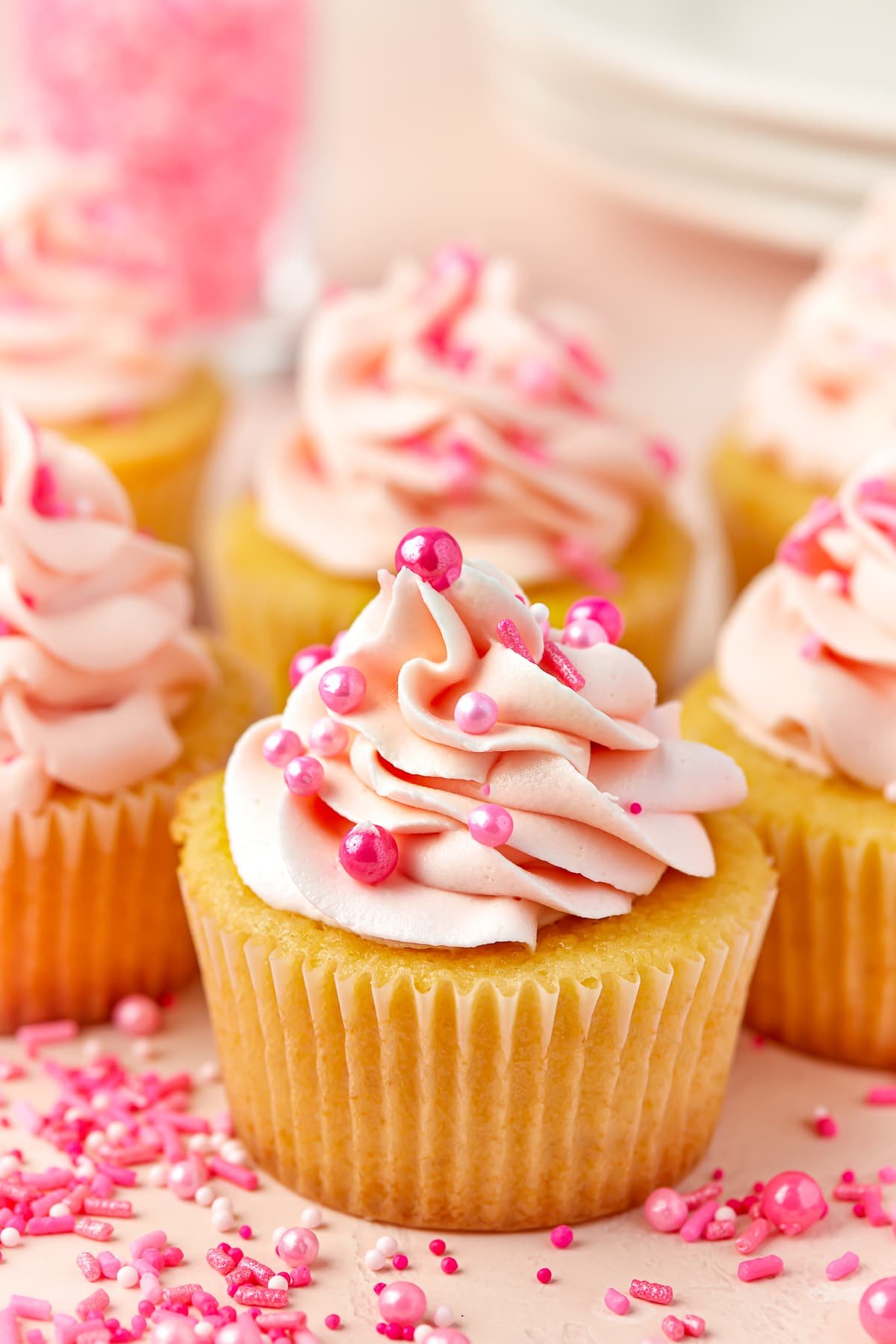 Valentine's Day Cupcakes grouped together with pink frosting and pink sprinkles, sitting on a pink tabletop