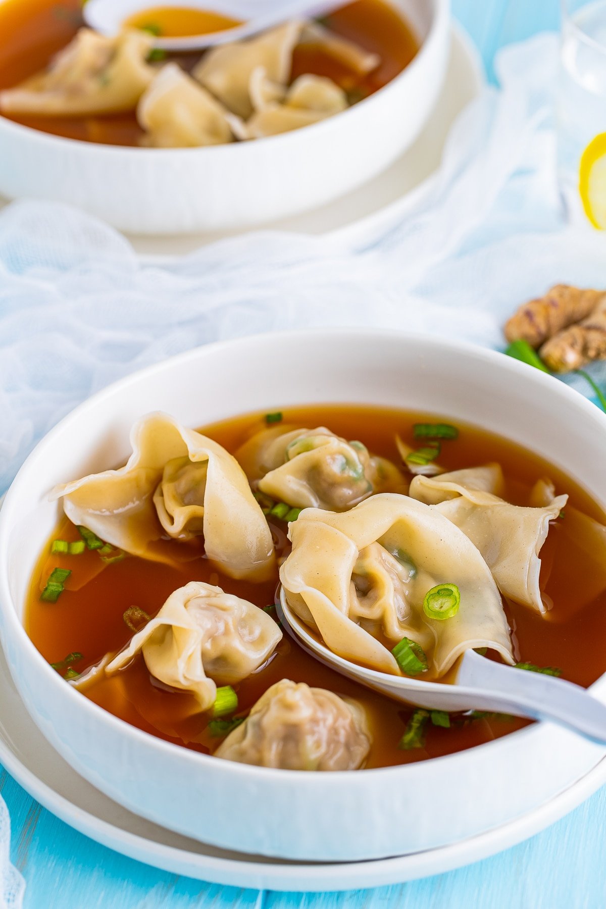 Wonton Soup Recipe in a white bowl with white spoon on bright blue background