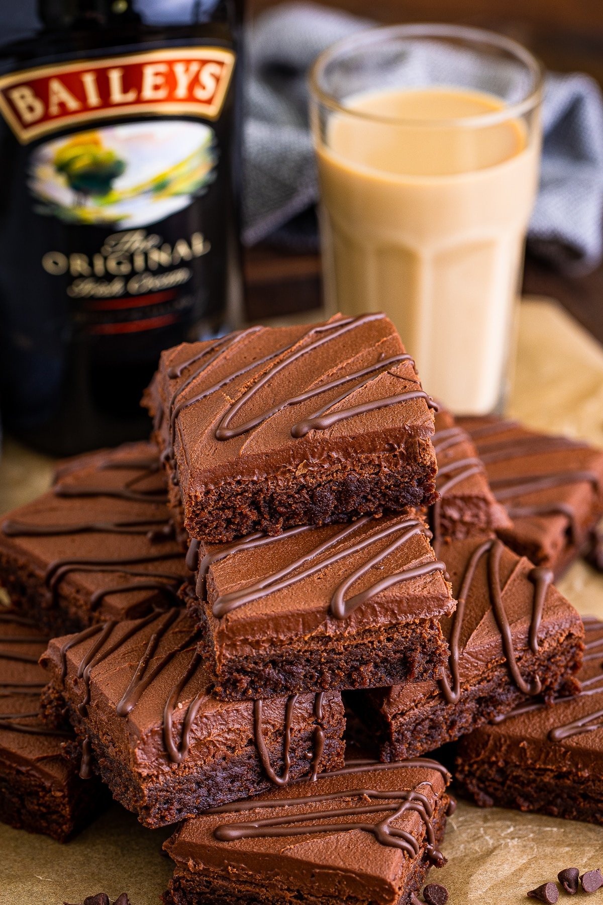 Bailey's Brownies stacked on brown parchment paper, a glass of Irish Cream and alcohol bottle in the background