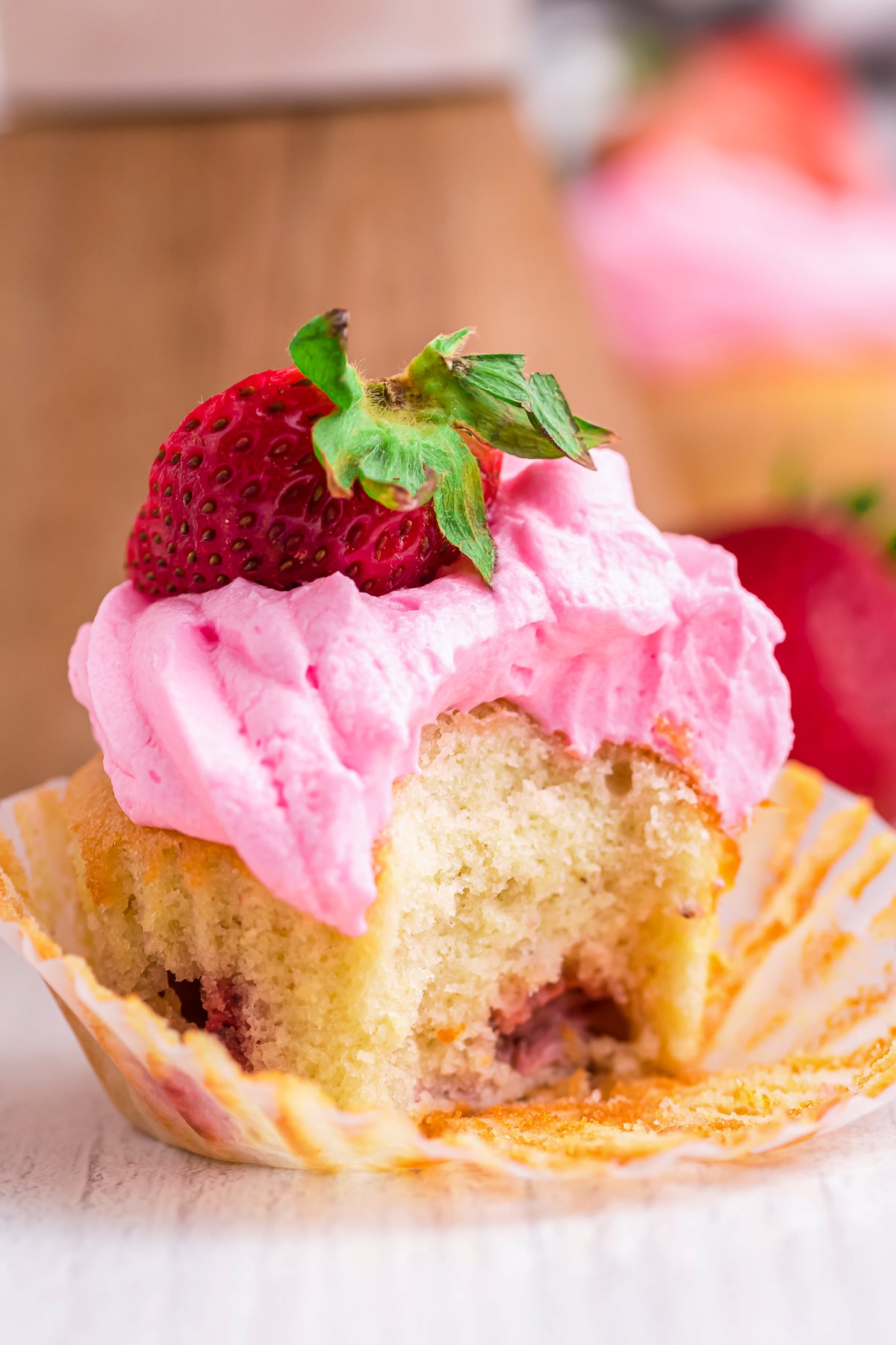 Photo showing a bite out of a Strawberry Cupcake on a white wooden table top