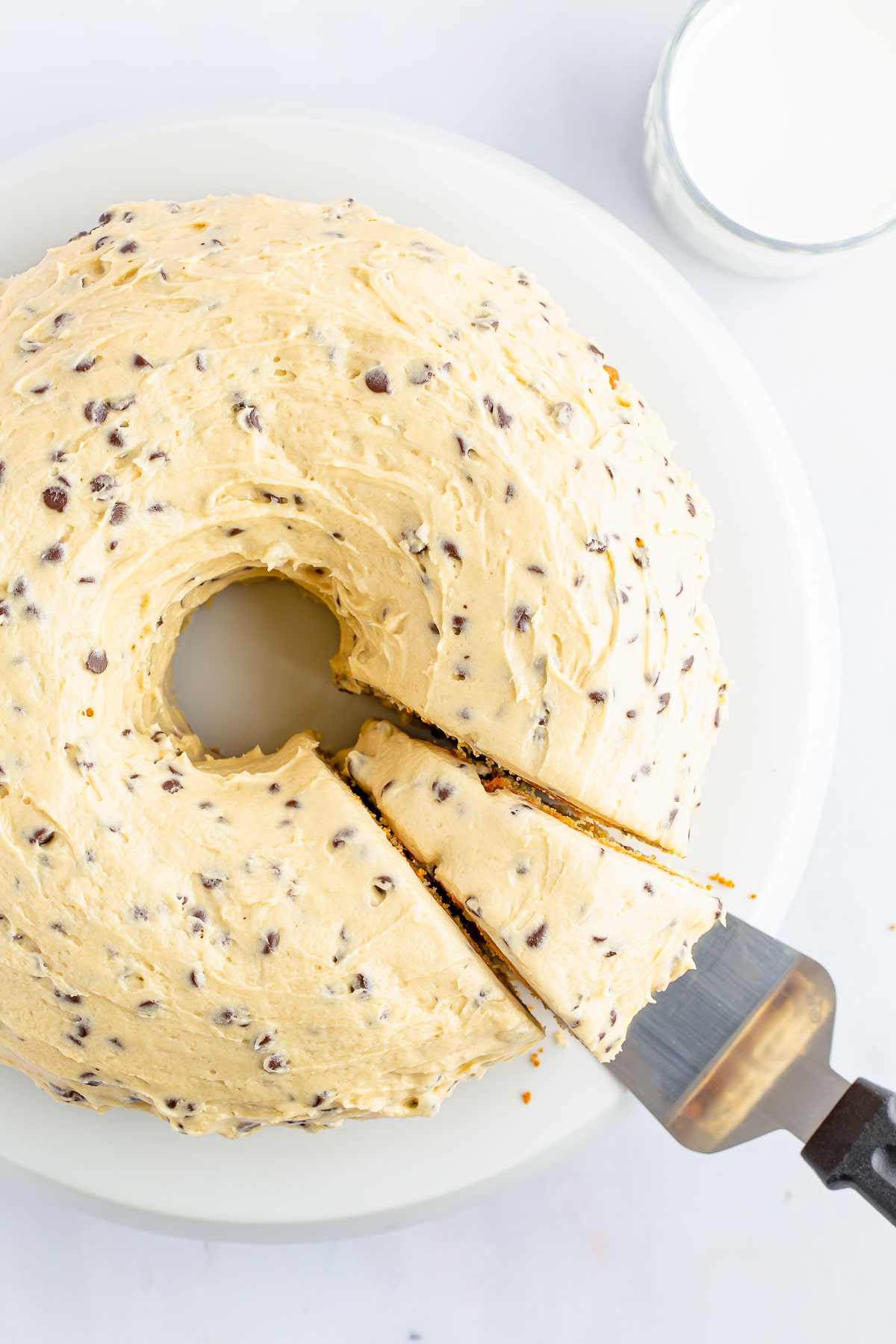 Overhead image of chocolate chip bundt cake with cake server taking a slice out, on white cake stand