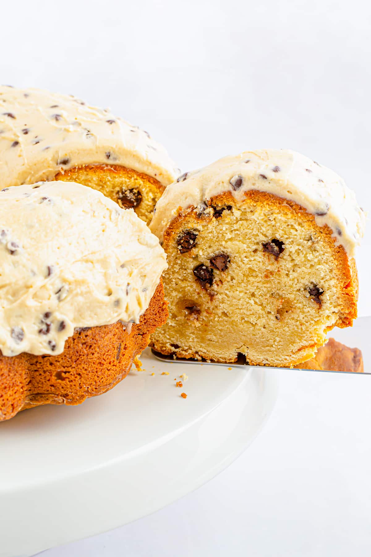 Upclose image of a slice of chocolate chip bundt cake coming out of the cake on a cake server, white cake stand