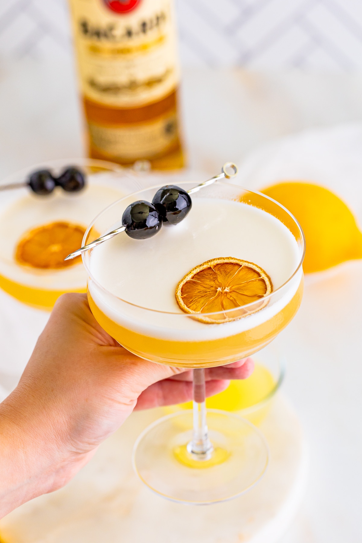 A hand holding a coupe glass with our rum sour recipe in a coupe glass