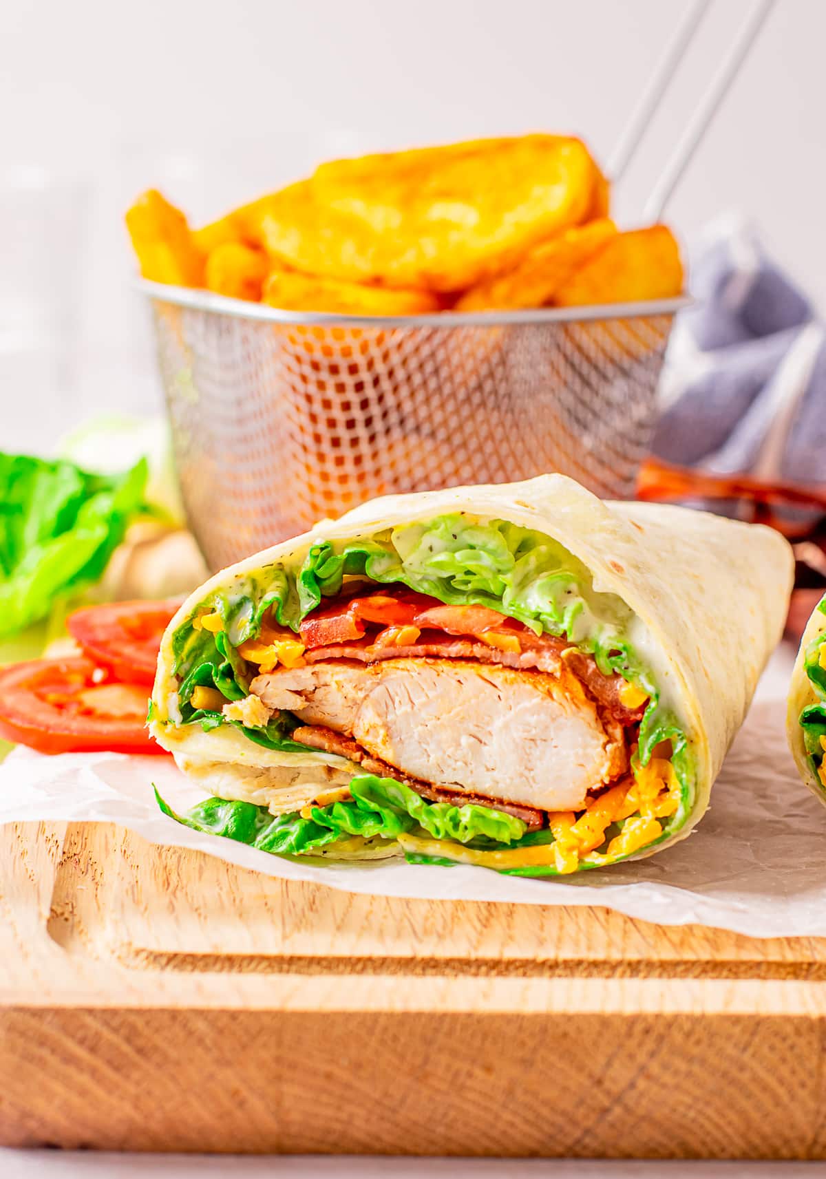 Upclose image of the interior of bacon ranch chicken wrap on a piece of white parchment paper sitting on a wooden cutting board.