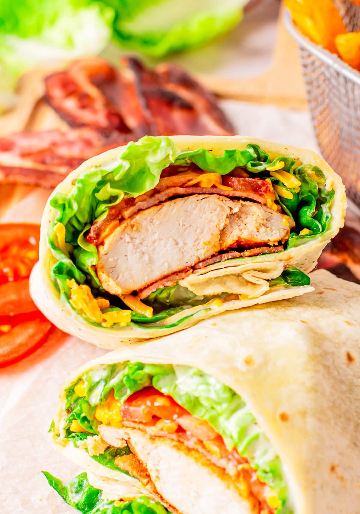 One piece of a cut bacon ranch chicken wrap propped up on another to show the interior. More bacon in the background.