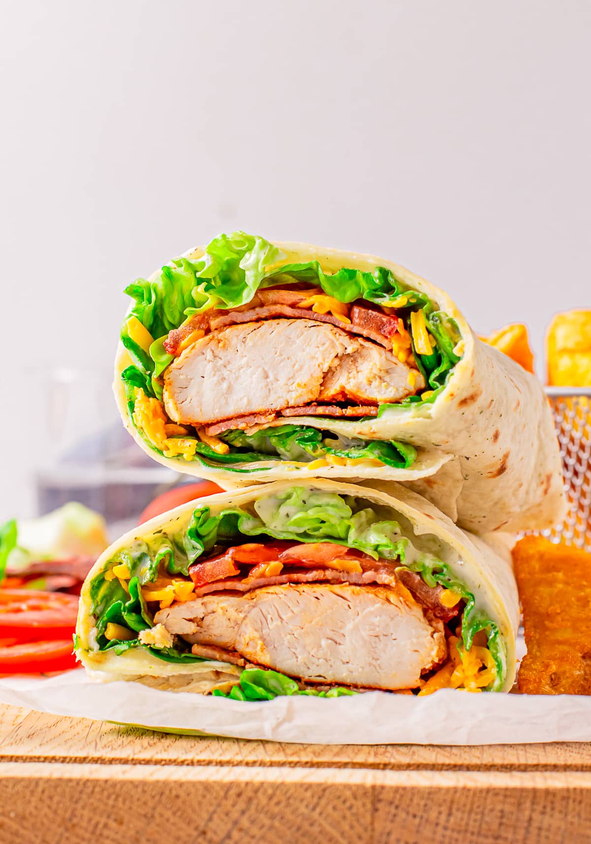 A bacon ranch chicken wrap cut in half to show the interior, two piece stacked on top of each other. Served on a wooden cutting board
