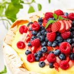 Sliced Pavlova Recipe topped with fresh berries, pastry cream, and whipped cream on a cake stand.
