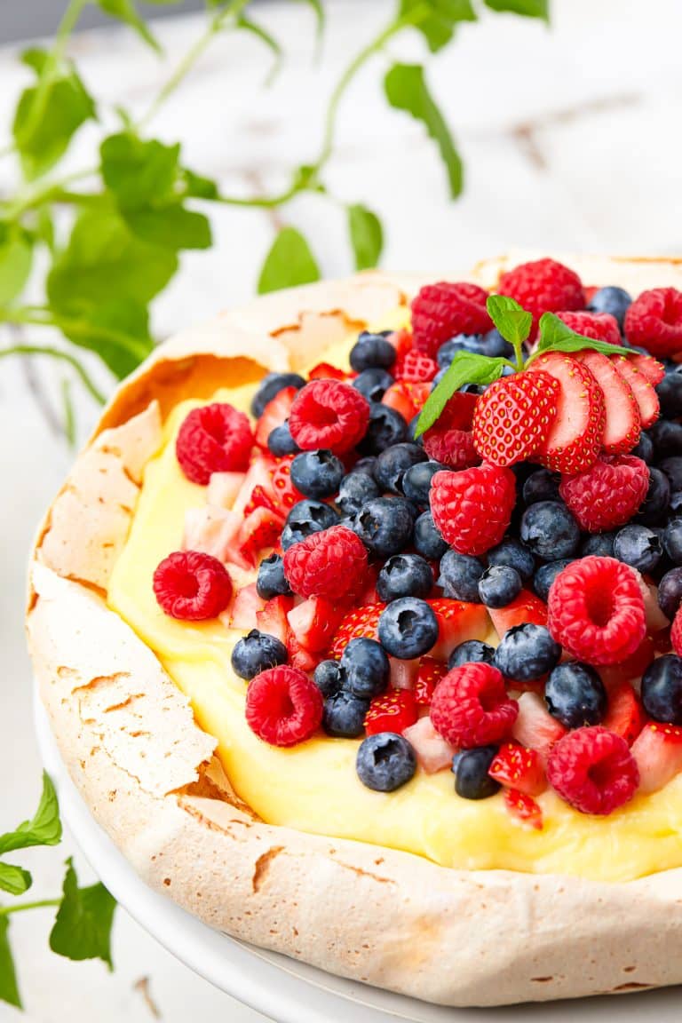 Sliced Pavlova Recipe topped with fresh berries, pastry cream, and whipped cream on a cake stand.