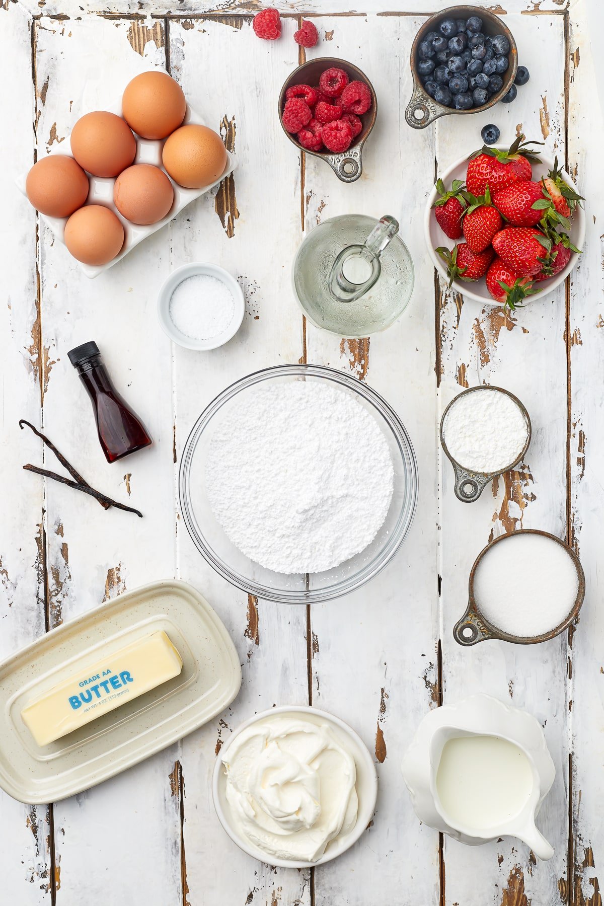 Overhead image of ingredients needed to make berry pavlova on a white wooden table top