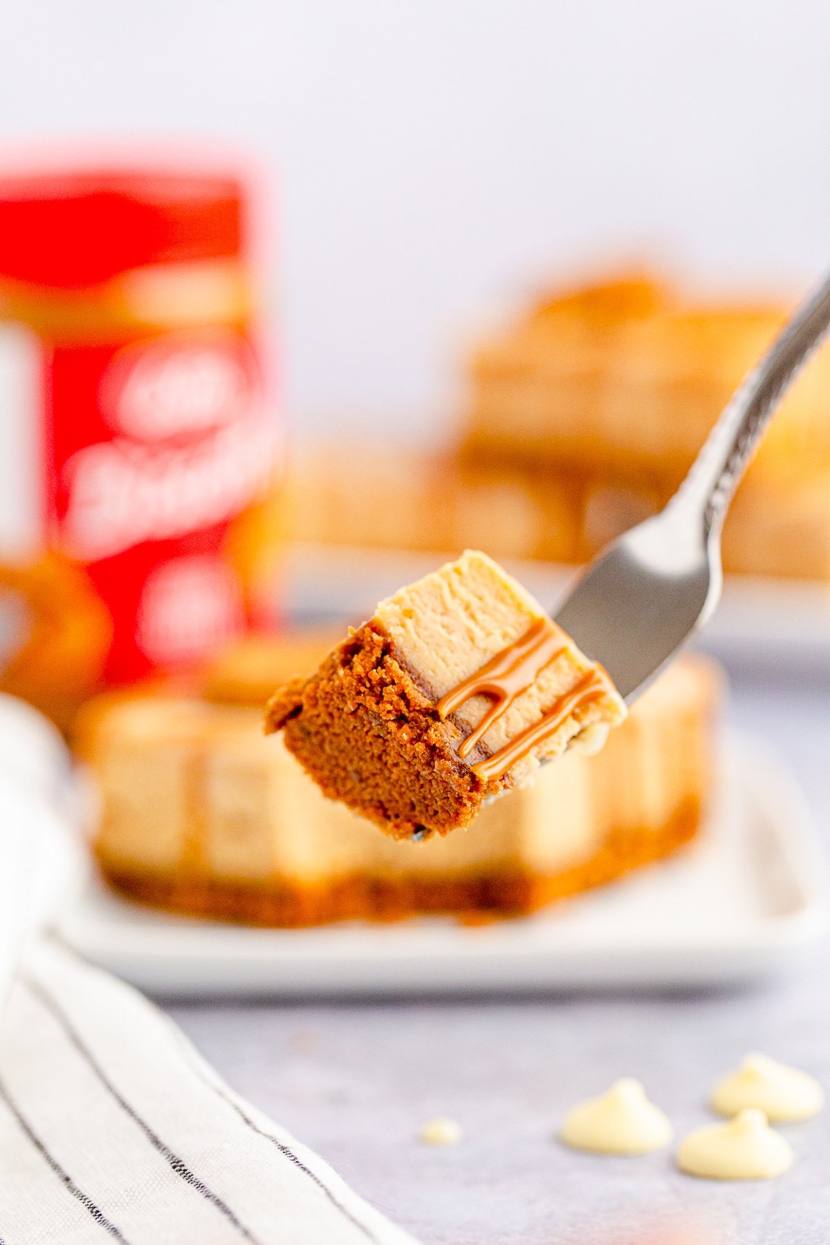 A piece of Biscoff Cheesecake Bars on a silver fork in air, blurred background of plated bars