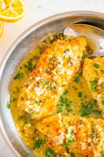 A skillet of cod piccata with golden pan-fried cod fillets in a lemon caper butter sauce topped with parsley.