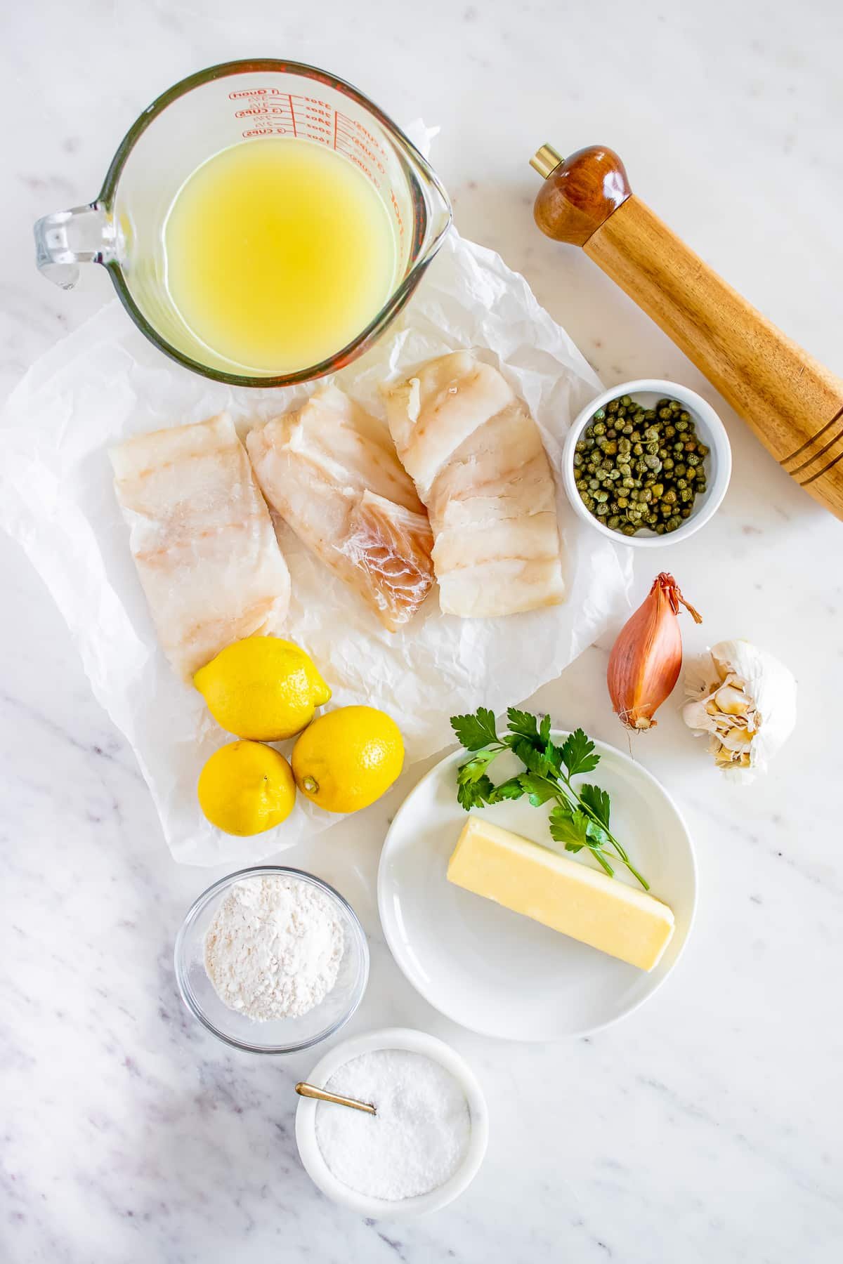 Overhead photo showing the ingredients needed to make fish piccata on a white marble table top