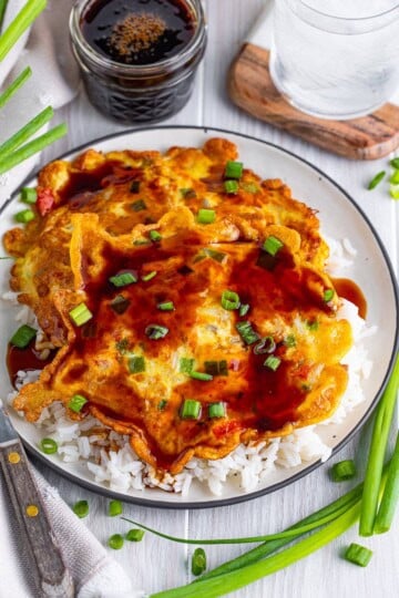 A plate of vegetable egg foo young topped with brown gravy and sliced green onions served over white rice.