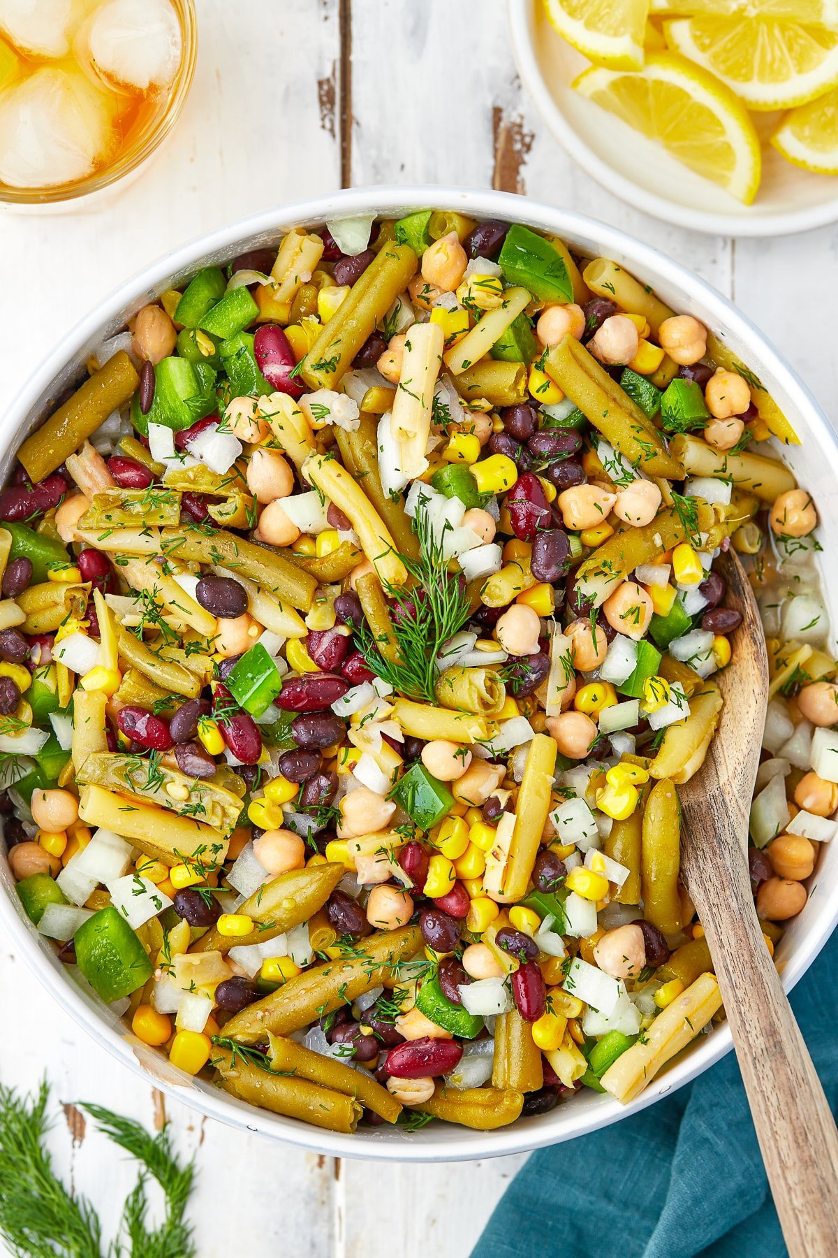 Overhead image of 5 bean salad in a white bowl with wooden spoon