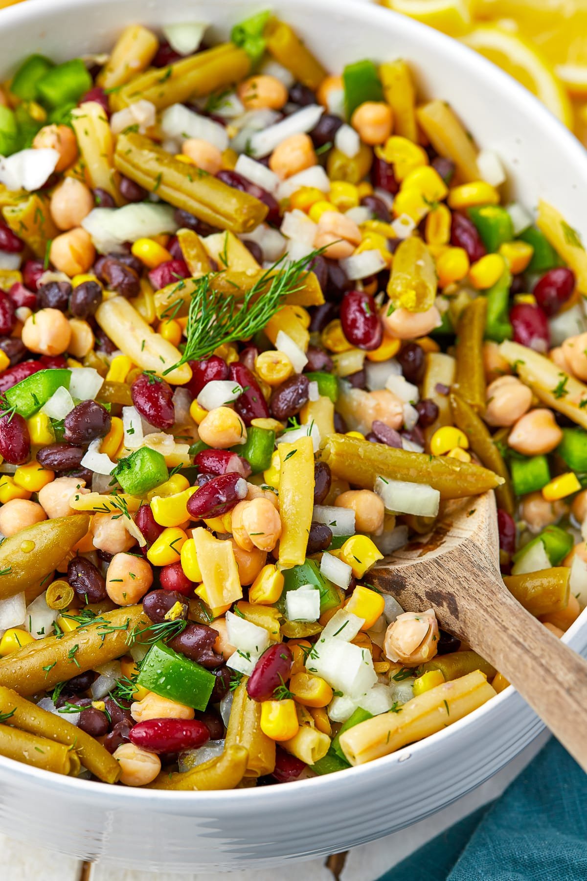 Up close image of 5 bean salad in a white bowl with a wooden spoon