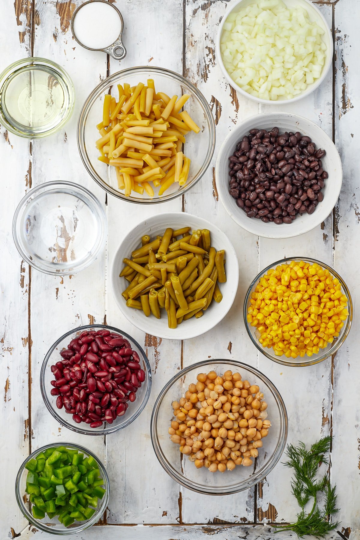 Overhead image of ingredients needed to make 5 bean salad on a white wooden table top