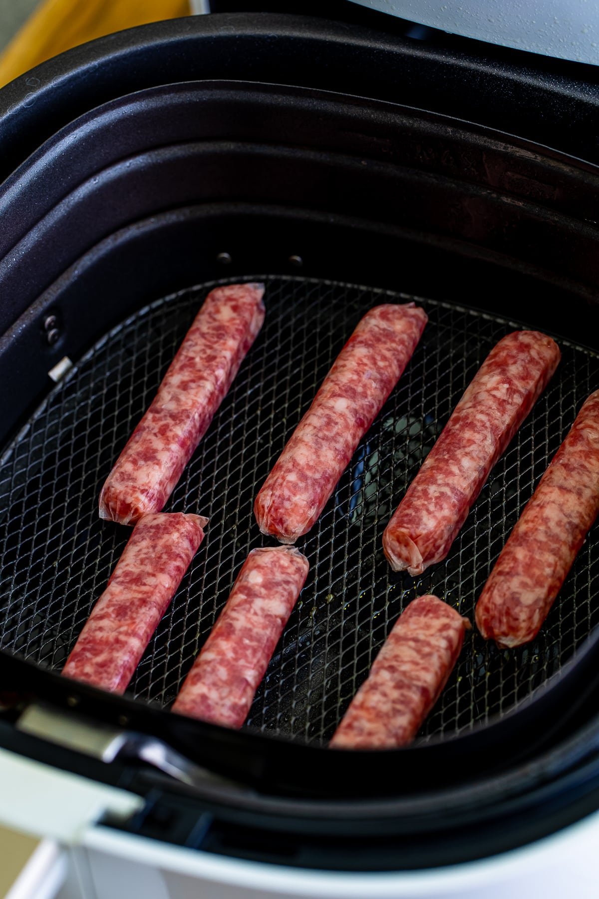 Raw breakfast sausage links sitting in a basket of a white air fryer