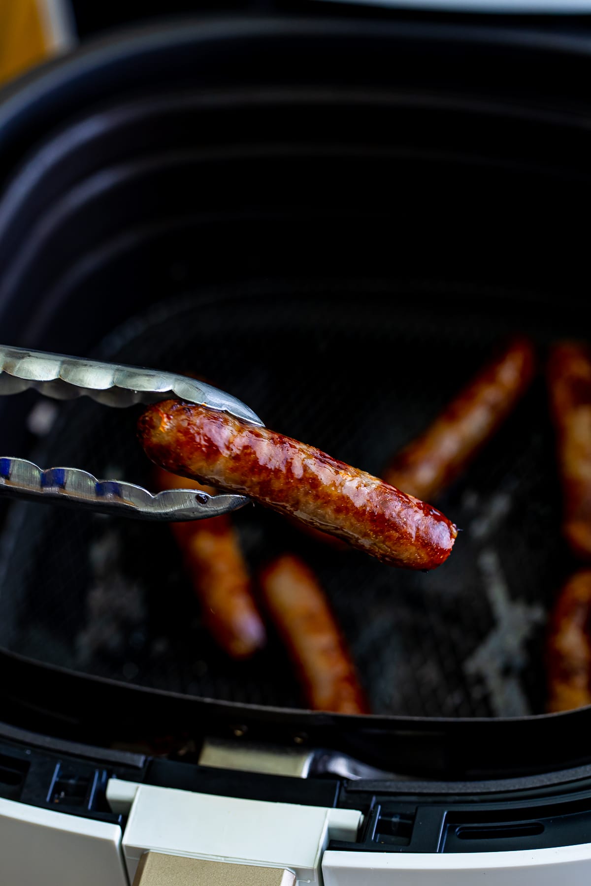 A silver tong holding up a cooked air fryer breakfast sausage link