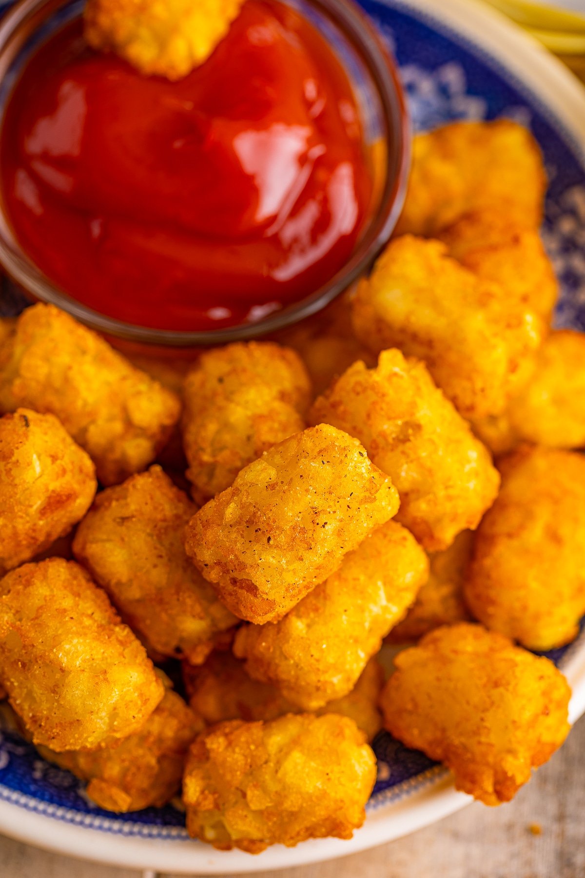 Overhead image of the best crispy air fryer tater tots on a blue plate with ketchup