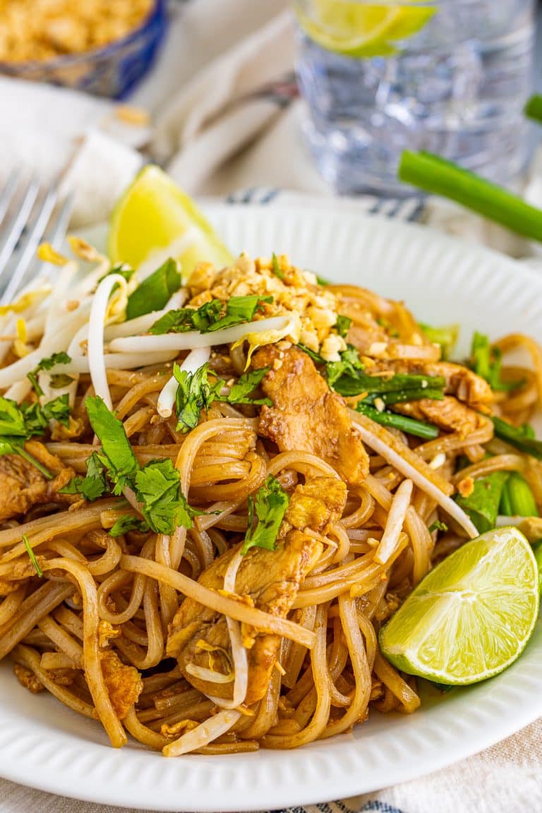 Spicy pad thai recipe with chicken on a white plate topped with bean sprouts, peanuts, and lime.