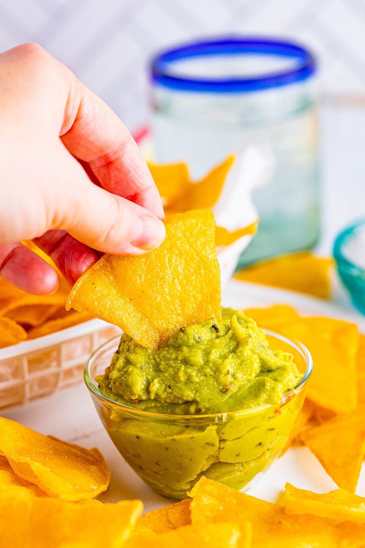 A hand holding a homemade fried tortilla dipping into guacamole