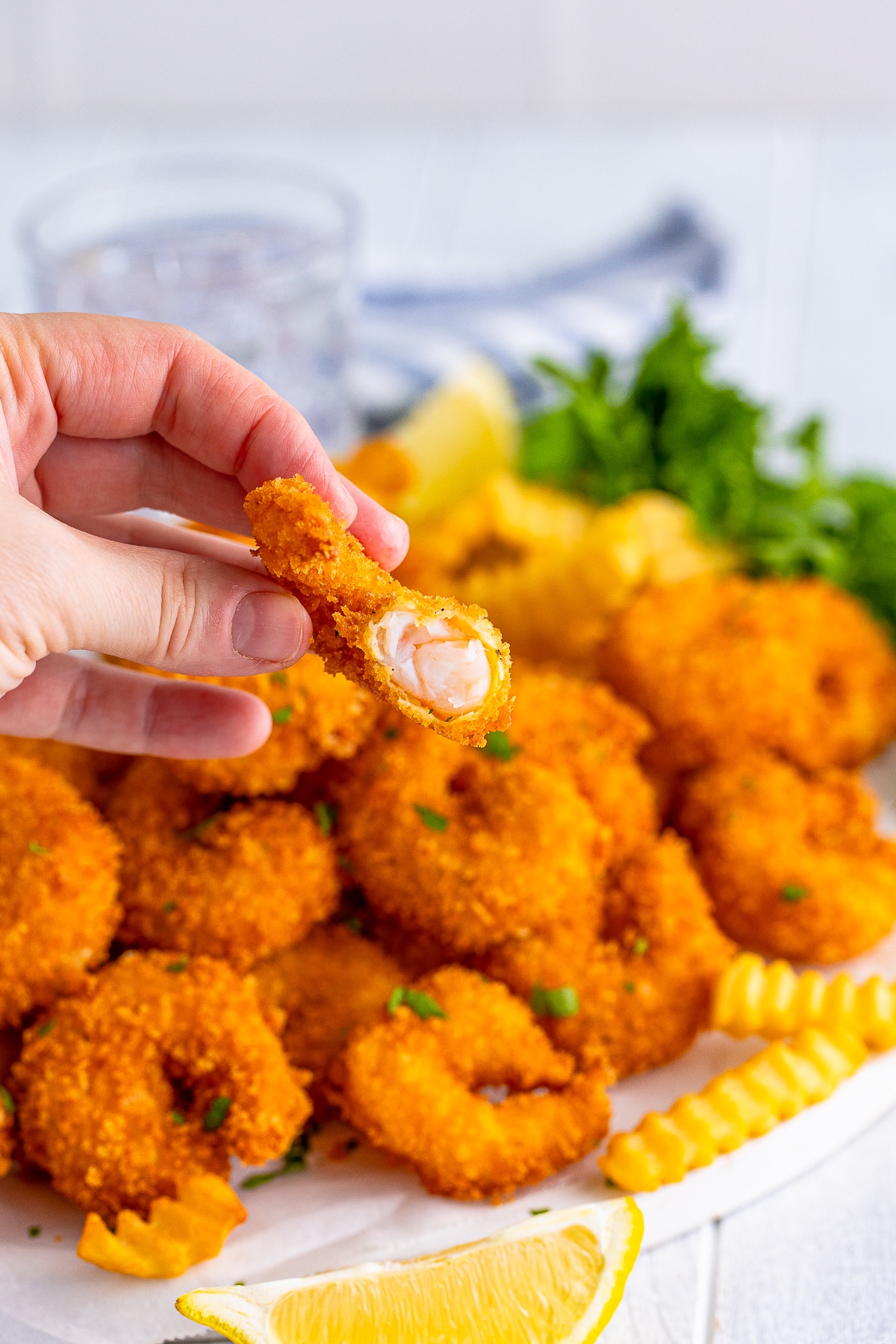 A hand holding a shrimp with a bite out of it to show the interior of panko shrimp