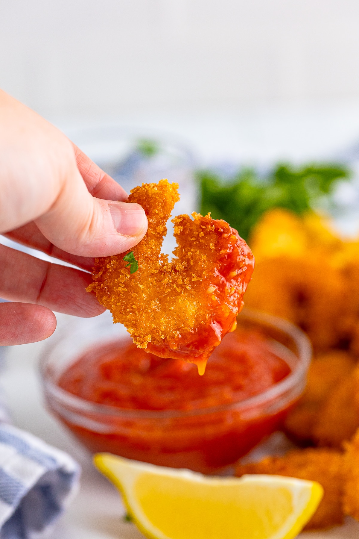 Hand in air showing a panko shrimp that was dipped in cocktail sauce