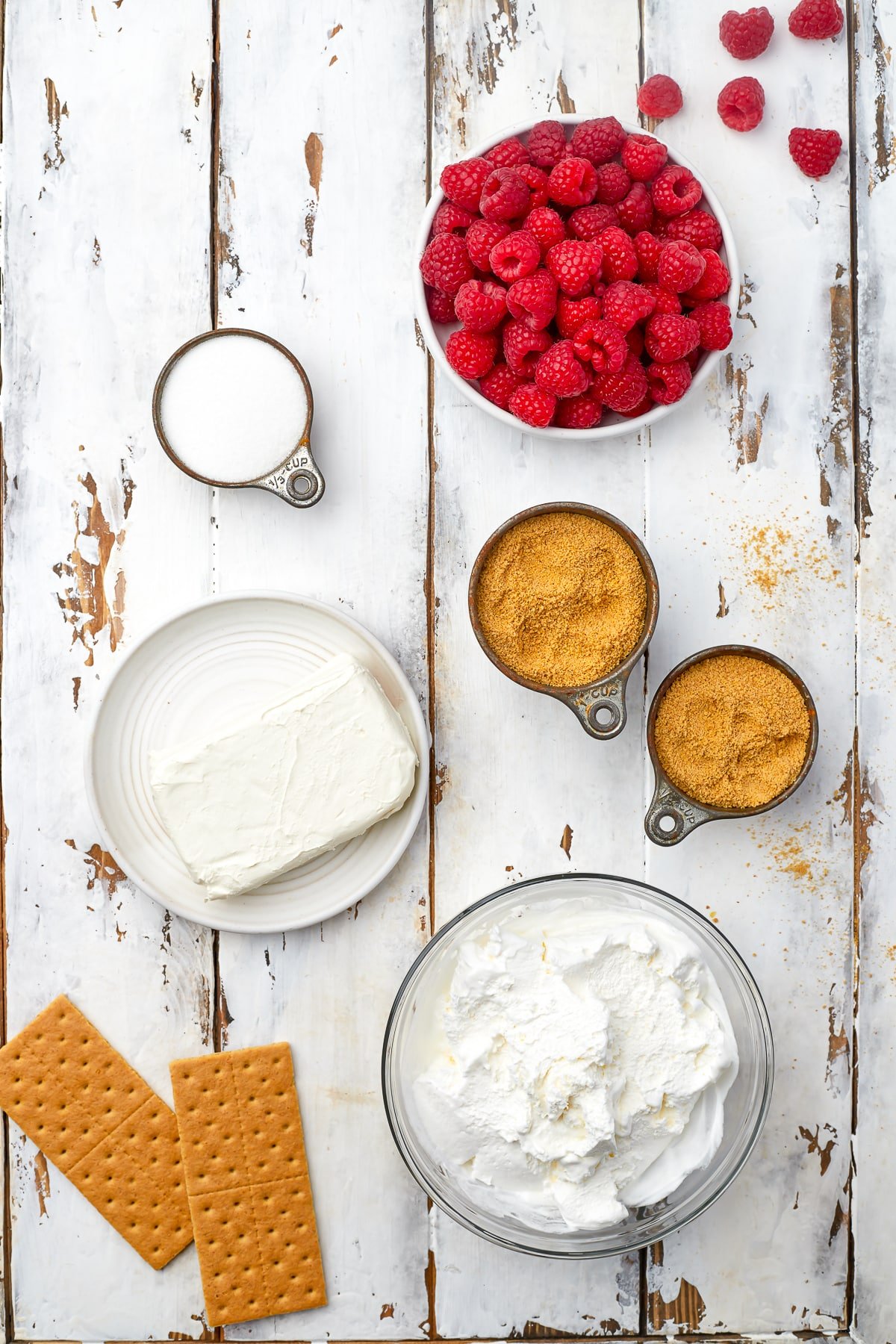 Overhead image showing ingredients needed to make no bake cheesecake bites on a white wooden table top