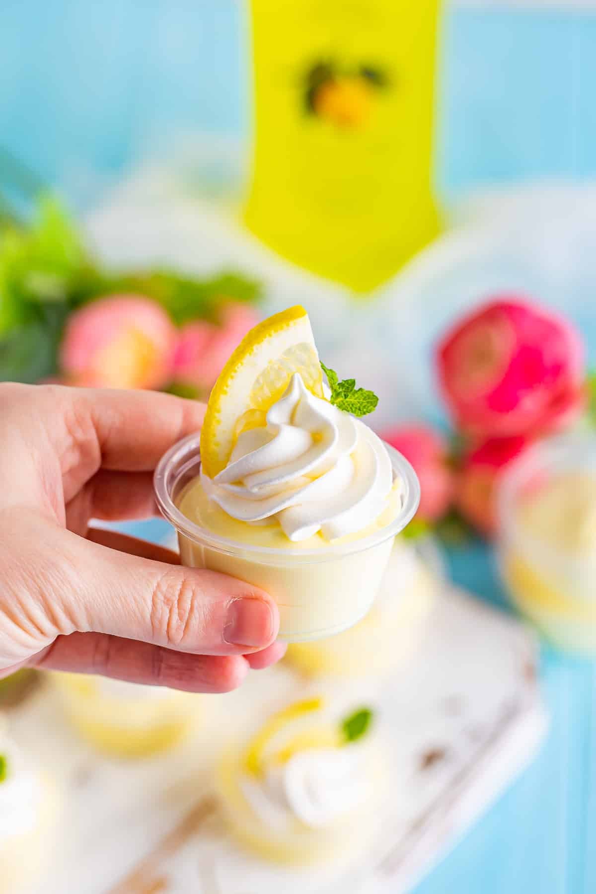 A hand holding a lemon pudding shot in air