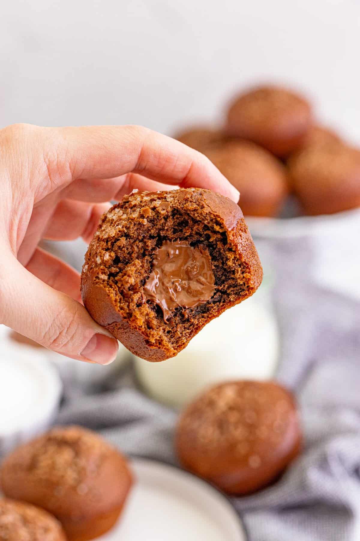 A hand holding a nutella muffin in air with a bite taken out to show the filling