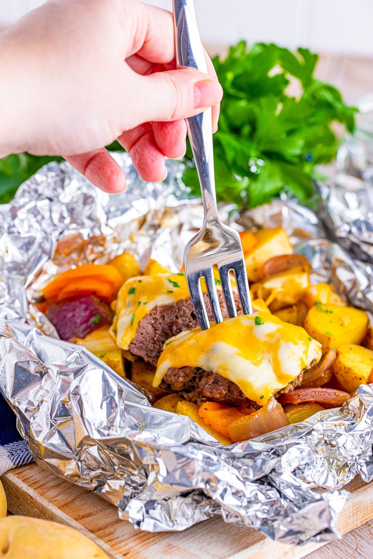 A hand with fork taking a piece of hamburger dinner foil packet from the packet