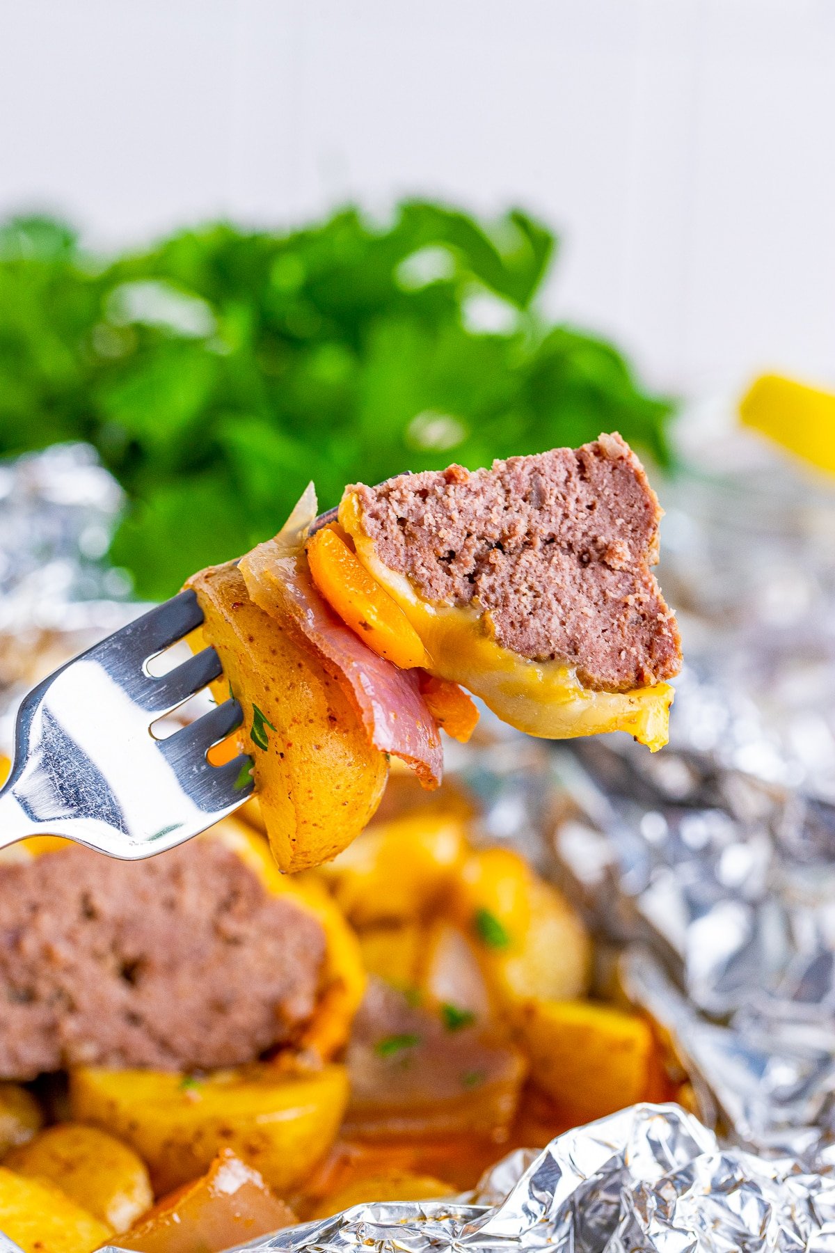 A silver fork in air showing a bite of hamburger dinner foil packet, parsley in background