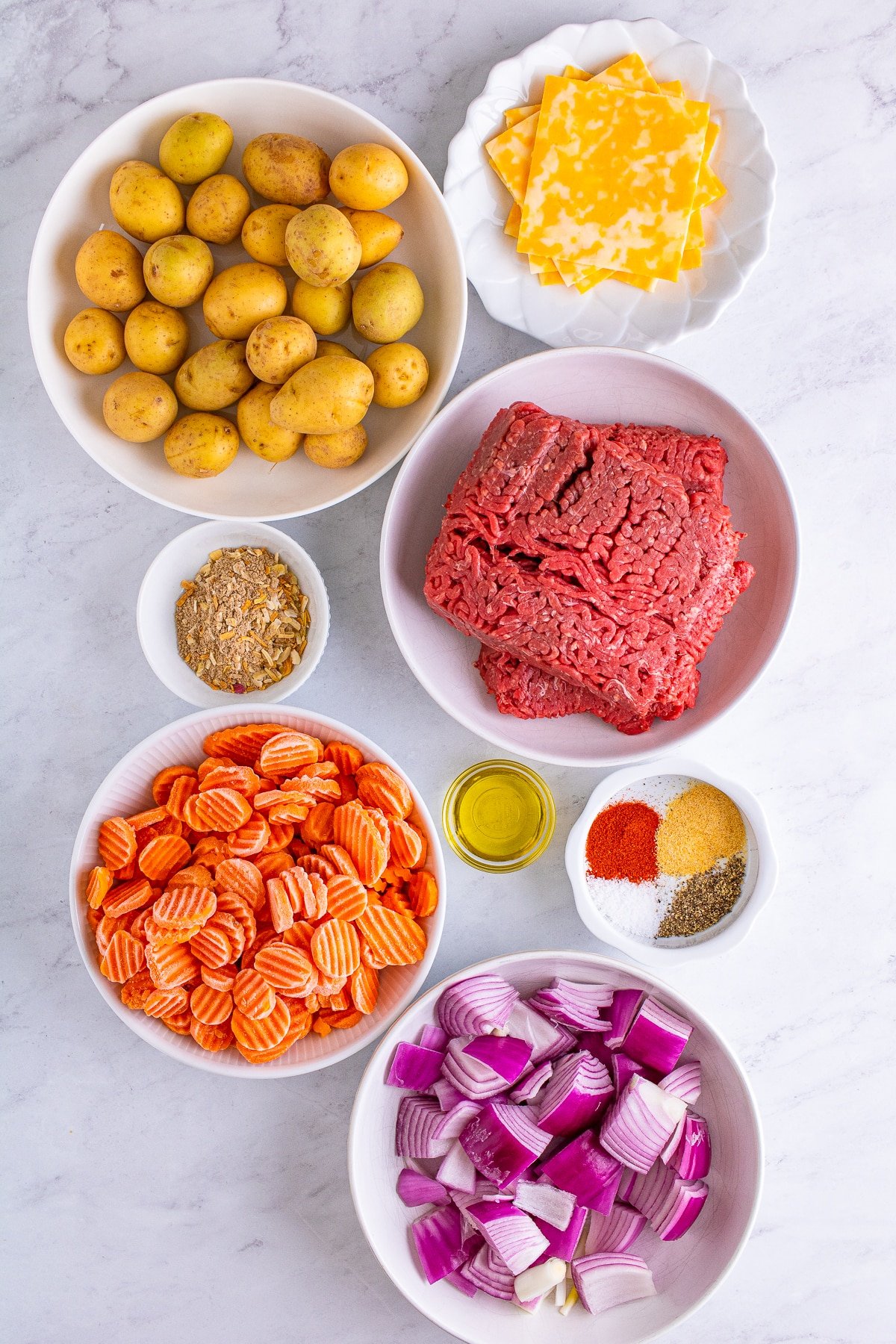 Overhead image showing the ingredients needed to make hamburger dinner foil packets on grey marble table top