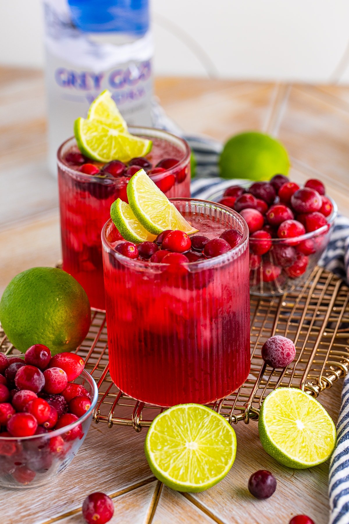 Further away image of vodka cranberry cocktail on a wire serving platter with cranberries and lime garnish
