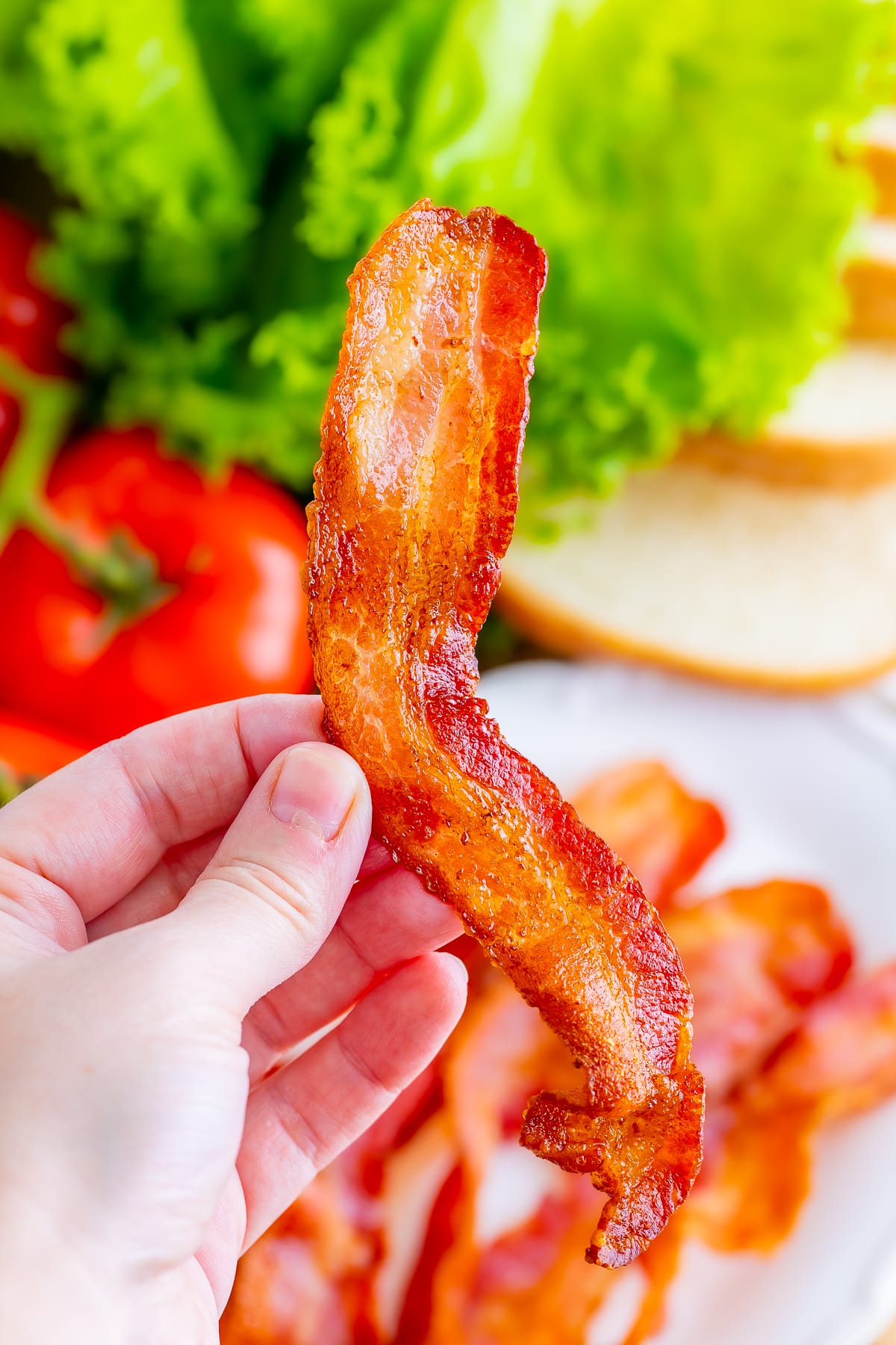 a hand holding a slice of bacon