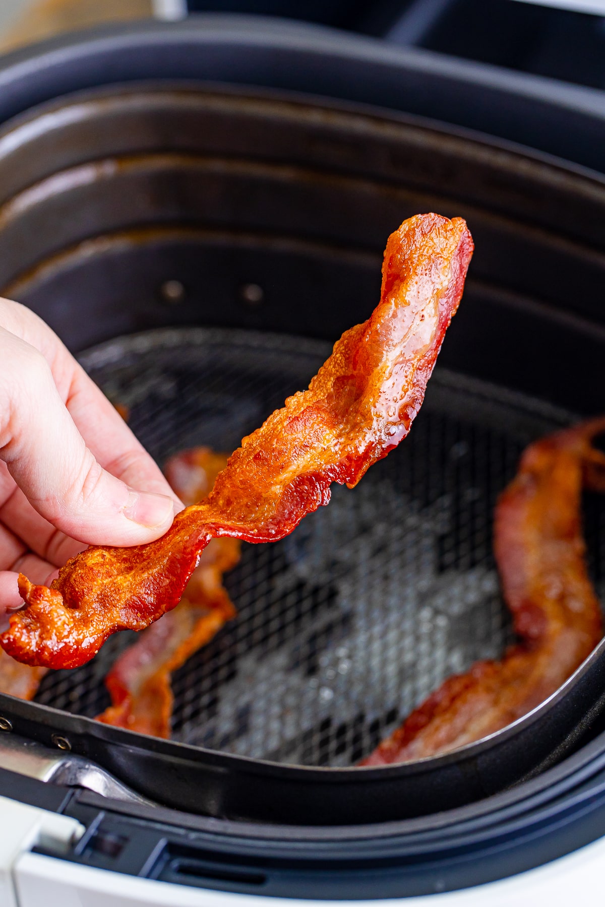 a hand holding a slice of air fryer bacon
